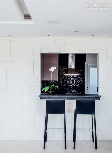 Entre sala e cozinha: há duas sugestões de emprego do drywall neste apartamento no interior de São Paulo, assinado pela arquiteta Érica Bragion, de Itatiba. A primeira tem efeito decorativo: na parede do passa-pratos, feita de alvenaria, instalaram-se placas simples, com três espessuras diferentes (2, 3,5 e 5 cm) e larguras variadas, para criar um jogo de volumes. A segunda aplicação está no forro, recortado para a instalação de spots e fitas de led.