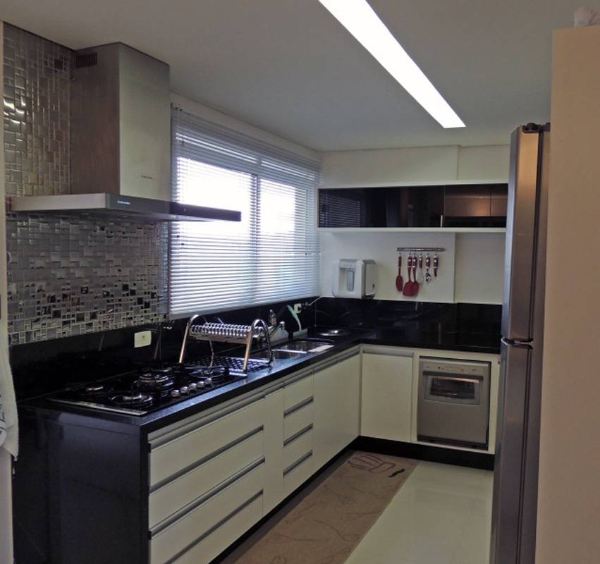 Se a cozinha tiver uma largura um pouco maior, d&aacute; para prolongar a bancada em L e usar a parede mais curta para instalar o forno. Neste projeto de Karina Correa, o filtro e um suporte para utens&iacute;lios de cozinha tamb&eacute;m ocupam o espa&ccedil;o.