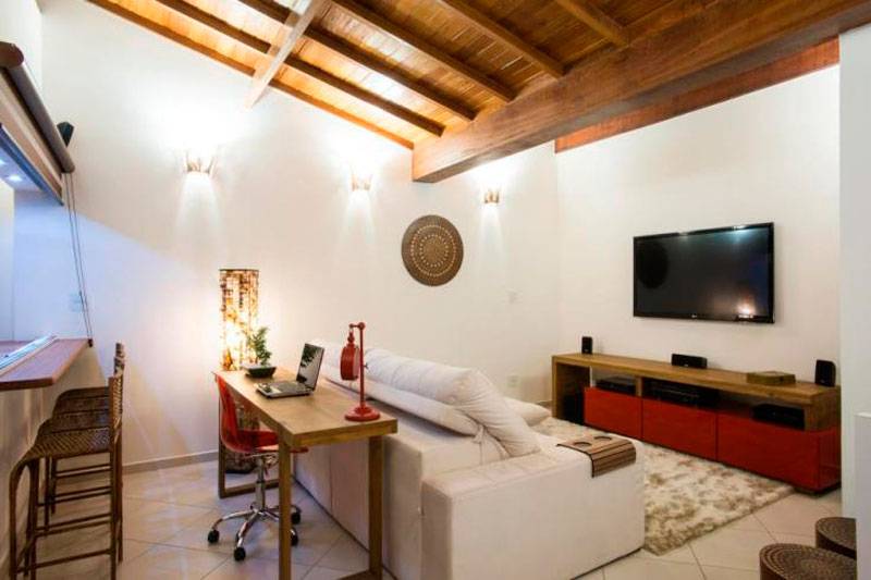 No segundo andar do apartamento, os moradores queriam um espa&ccedil;o para assistir televis&atilde;o, receber os amigos e usar o notebook. A arquiteta Luciana Lopes ent&atilde;o integrou o espa&ccedil;o de 20 m&sup2; com a varanda gourmet por meio de uma bancada &ndash; que pode ser visualizada do lado direito da foto &ndash; al&eacute;m de aproveitar o aparador atr&aacute;s do sof&aacute; como suporte para o notebook.
