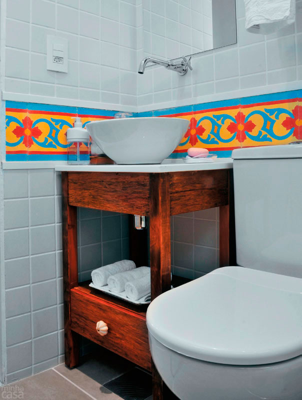 Um gracioso m&oacute;vel de peroba-rosa de demoli&ccedil;&atilde;o desenhado sob medida para caber ao lado do vaso sanit&aacute;rio substitui a pia de porcelana neste banheiro. A arquiteta Lucilla Almeida escolheu um tampo de nanoglass e arrematou o ambiente com uma faixa de ladrilhos hidr&aacute;ulicos.