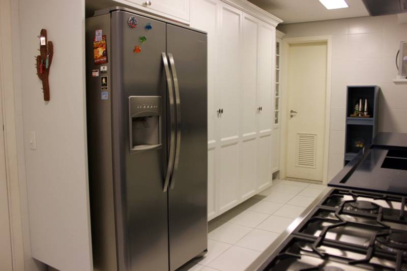 Arm&aacute;rios suspensos com um design que remete &agrave; guarda-roupas de quartos comp&otilde;em uma das paredes desta cozinha projetada por Nataly Aguiar.
