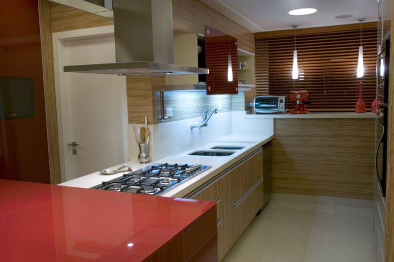 Apesar do layout irregular, esta cozinha projetada por Elizabete Nunes Botsaris segue os mesmo padr&otilde;es de uma estilo corredor: cooktop e pia de um lado, geladeira e fornos do outro. Para integrar tudo, a parede recebeu o mesmo revestimento amadeirado dos arm&aacute;rios.
