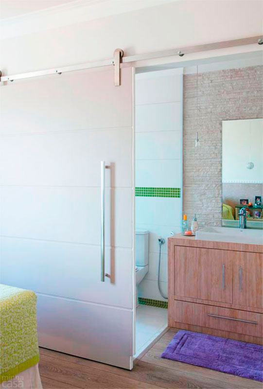 O espa&ccedil;o em que fica a bancada foi planejado para receber um minicloset, mas a arquiteta Josanda Ferreira rejeitou a ideia e estendeu o piso laminado do quarto at&eacute; o lavat&oacute;rio. Uma porta de correr conecta o banheiro e o dormit&oacute;rio com muita classe e isola os ambientes quando desejado.