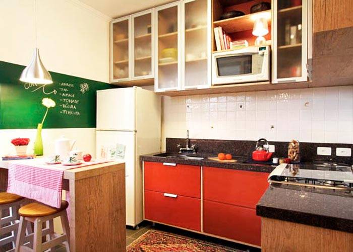 A cozinha projetada pela arquiteta Thais Lenzi Bressiani utiliza o vermelho no arm&aacute;rio e em diversos acess&oacute;rios . Na parede, uma tinta que imita lousa &eacute; utilizada para anotar recados e receitas. Para n&atilde;o pesar no ambiente, os arm&aacute;rios ganharam portas transl&uacute;cidas.