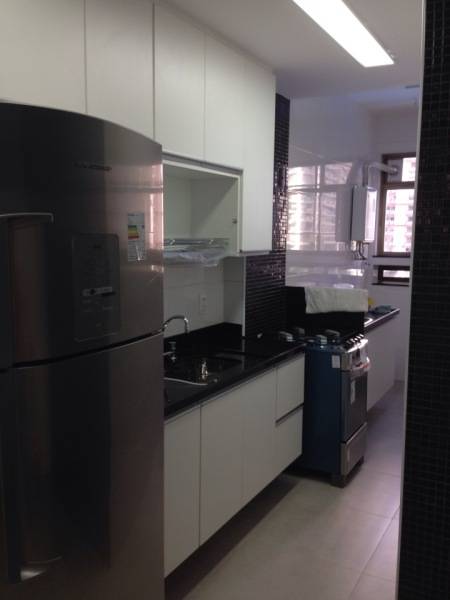 Detalhes em preto na parede do fog&atilde;o complementam o uso da cor na pedra da bancada. Esta cozinha, projetada por Rita de C&aacute;ssia Mendes Trica, &eacute; integrada &agrave; &aacute;rea de servi&ccedil;o, que &eacute; delimitada por uma meia parede.