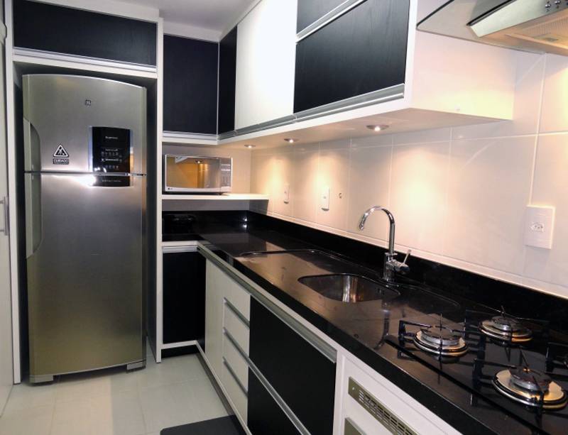 Mesmo com uma &aacute;rea estreita, o escrit&oacute;rio Frente Verso Arquitetura conseguiu acomodar tudo nesta cozinha: a parede menor abriga a geladeira e o forninho. Os arm&aacute;rios em preto e branco criam um bom efeito visual.