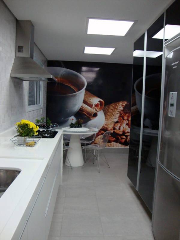 Esta cozinha projetada pelo escrit&oacute;rio Madi Arquitetura e Design termina em uma &aacute;rea de refei&ccedil;&otilde;es que recebeu uma plotagem na parede. As cores da foto ao fundo se repetem na parte da bancada.
