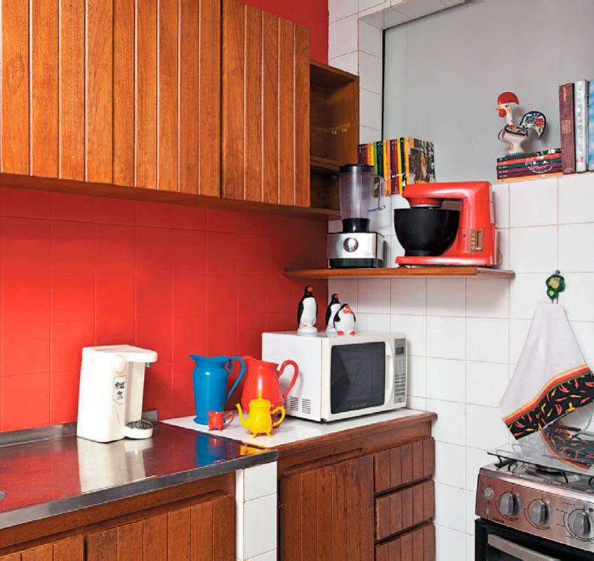Jarras e a&ccedil;ucareiros velhinhos conquistaram visual pop na cozinha ap&oacute;s um banho de cor. Os azulejos brancos receberam uma camada de tinta vermelha, que contrastou com os arm&aacute;rios de madeira e com a geladeira de inox. Projeto de Valentina Rocha.
