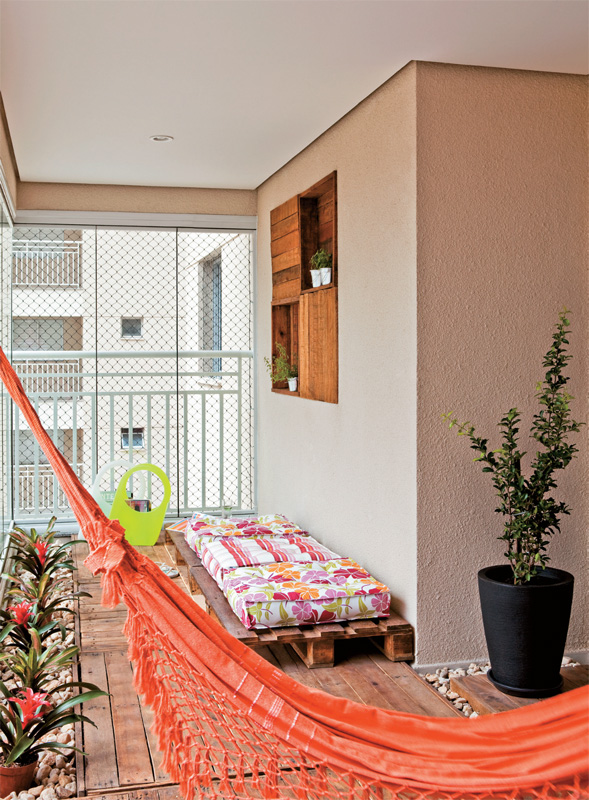 Rede em varanda zen. Neste amplo terra&ccedil;o (6,90 x 2,40 m), foi montado um espa&ccedil;o zen. Para trazer o aconchego da madeira, as designers Cec&iacute;lia Guerra e Cristiane Tamburri, sua s&oacute;cia no escrit&oacute;rio Duo C Design, encomendaram paletes, lixados e envernizados, que fazem as vezes de deque. A rede &eacute; um espa&ccedil;o para descanso em meio &agrave; paisagem da cidade grande e sua cor dialoga com a dos estofados e as flores.