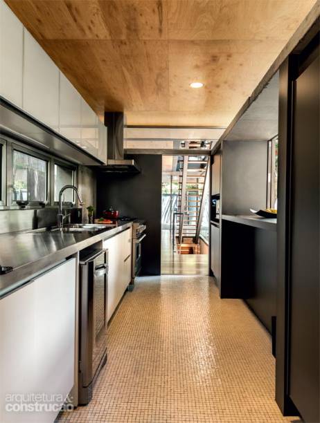 A cozinha foi idealizada com um passa-pratos para a sala, fechado por porta de correr. O piso revestido de mosaicos de vidro se alia ao laminado cinza que cobre as paredes de alvenaria e à bancada de inox (Mekal). Projeto do arquiteto Fernando Viegas.