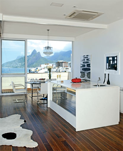 22 m&sup2;: A vista do mar e do morro Dois Irm&atilde;os determinou o projeto da arquiteta carioca Roberta Moura para esta cobertura: de olho na paisagem, ela cercou o espa&ccedil;o com pain&eacute;is de correr de vidro. E, ao criar um ambiente &uacute;nico de estar, destacou a cozinha gourmet  delimitada pela ilha de 2,30 x 1,10 m, revestida de m&aacute;rmore branco extra, que acomoda uma cuba de a&ccedil;o inox e um fog&atilde;o cooktop. O piso de t&aacute;buas de ip&ecirc; com 10 cm de largura foi aproveitado do deck que cobria o antigo terra&ccedil;o e intercalado com pequenas ripas de garapa. Ele resiste bem aos p&eacute;s molhados de quem sai da ducha existente na parte descoberta, garante Roberta.