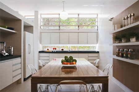 63 m&sup2;: Copa de um lado, cozinha do outro. Para dividi-las, uma estrutura de alvenaria j&aacute; existente no projeto original da casa paulistana, erguida em 1966 e reformada 40 anos depois pelo arquiteto Leonardo Junqueira. Como h&aacute; espa&ccedil;o de sobra e os novos propriet&aacute;rios queriam manter a separa&ccedil;&atilde;o entre os ambientes, aproveitei essa parede central para embutir arm&aacute;rios e eletrodom&eacute;sticos, conta o autor, que a revestiu de pastilhas de porcelana brancas em formato palito, de 2,5 x 5 cm. A obra tamb&eacute;m facilitou a circula&ccedil;&atilde;o, gra&ccedil;as &agrave; retirada de um balc&atilde;o que formava um grande U e ocupava boa parte da &aacute;rea onde hoje se encontra a mesa, recanto preferido pela fam&iacute;lia para os caf&eacute;s-da-manh&atilde;. Achei melhor deixar as bancadas com pias apenas sob as janelas, explica Leonardo.