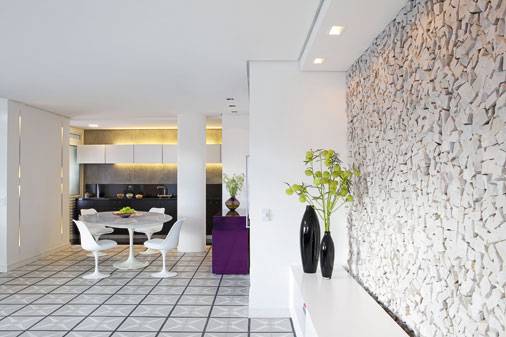 Destaque dos ambientes, o m&oacute;vel preto da cozinha possui todos os eletrodom&eacute;sticos necess&aacute;rios embutidos. Nele, &eacute; sobreposta uma pe&ccedil;a de granito preto que segue na parede de cimento queimado. A ilumina&ccedil;&atilde;o arremata a decora&ccedil;&atilde;o do ambiente, integrado com a sala pelo branco da pe&ccedil;a de ambos os espa&ccedil;os.