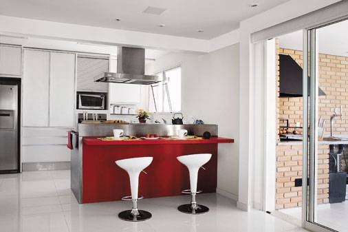 A reforma deste apartamento derrubou a parede que separava a cozinha da sala. No lugar, uma bancada funcional de a&ccedil;o inox d&aacute; espa&ccedil;o para cooktop, escorredor e outros objetos. Atrelado a bancada, um aparato de MDF com pintura grofato vermelha disponibiliza dois lugares para refei&ccedil;&otilde;es r&aacute;pidas.