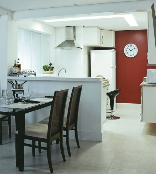 Na reforma deste apartamento, uma parede derrubada integrou a cozinha a sala. Ao lado da bancada de MDF, placas de porcelanato no piso integram os ambientes. A decora&ccedil;&atilde;o clean &eacute; contrastada pelo vermelho da parede.