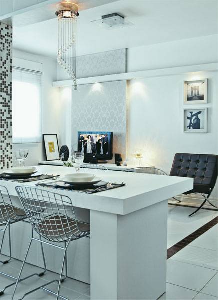 Nesta cozinha, uma mesa sobrep&otilde;e a bancada. A base desta mesa aproveita a parte inferior das paredes parcialmente demolidas na reforma. O piso, a parede e os m&oacute;veis de ambos ambientes foram revestidos de branco: al&eacute;m de dar unidade ao espa&ccedil;o, este &eacute; um recurso que proporciona amplitude ao apartamento de 50 m&sup2; .