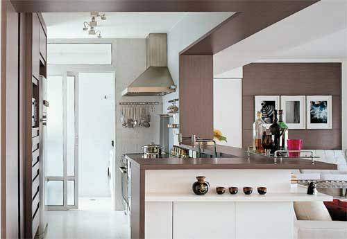 Na cozinha, a prancha de madeira da bancada continua na parede e no teto, criando uma moldura. A mesma madeira &eacute; utilizada na sala, criando unidade visual para a &aacute;rea integrada. Reforma realizada pelos arquitetos Fl&aacute;vio Butti e Alice Martins.