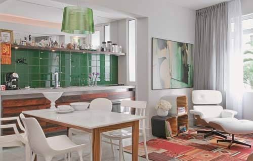 Neste apartamento de 57 m&sup2;, cozinha e sala &eacute; uma coisa s&oacute;. As &aacute;reas s&atilde;o diferenciadas pelas cores marcantes, como o verde escuro do azulejo da cozinha. O contraste fica por conta do tapete da sala, em tons quentes.