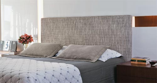 Amplos pain&eacute;is laqueados e entremeados de recortes com ilumina&ccedil;&atilde;o embutida (Marcenaria Clamom M&oacute;veis) formam uma base moderna e, ao mesmo tempo, neutra no quarto do casal, projetado pelo arquiteto Toninho Noronha. O recurso &eacute; ideal para destacar o mobili&aacute;rio desenhado pelo pr&oacute;prio arquiteto, como a cabeceira, feita sob medida pela Tre Uni Tape&ccedil;aria. &ldquo;Com base de madeira estofada e revestida de l&atilde; tramada da Interni, a pe&ccedil;a &eacute; fixada diretamente na parede para ficar firme e deixar a cama box livre&rdquo;, explica Noronha. A colcha e as almofadas s&atilde;o de seda r&uacute;stica cinza do Emp&oacute;rio Beraldin.
