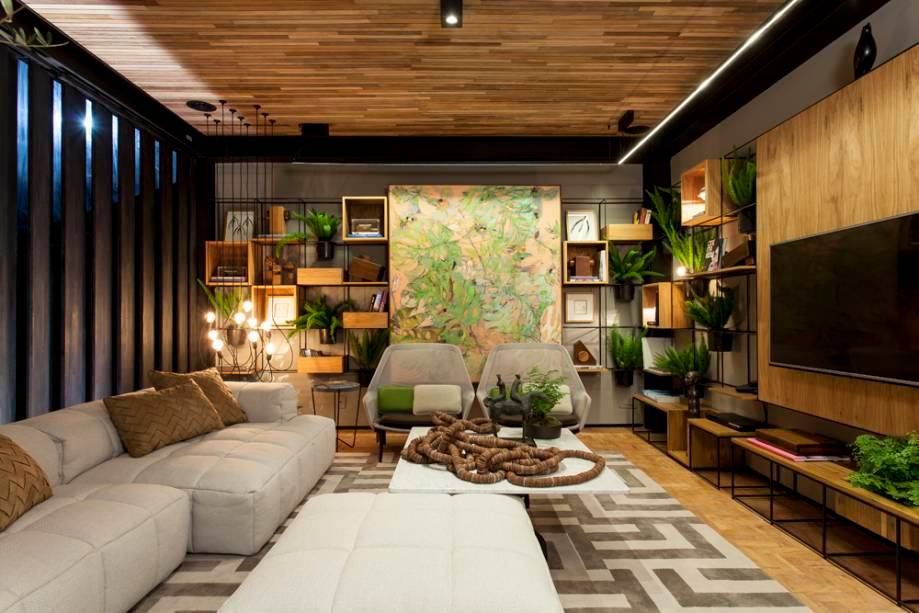 O projeto da arquiteta La&iacute;s Galv&atilde;o agrega design nacional e internacional, al&eacute;m de valoriza a arte e a cultura local com muita eleg&acirc;ncia e conforto. Com ilumina&ccedil;&atilde;o natural da medida, o verde foi explorado atrav&eacute;s das plantas distribu&iacute;das nos nichos da estante que envolve a sala.
