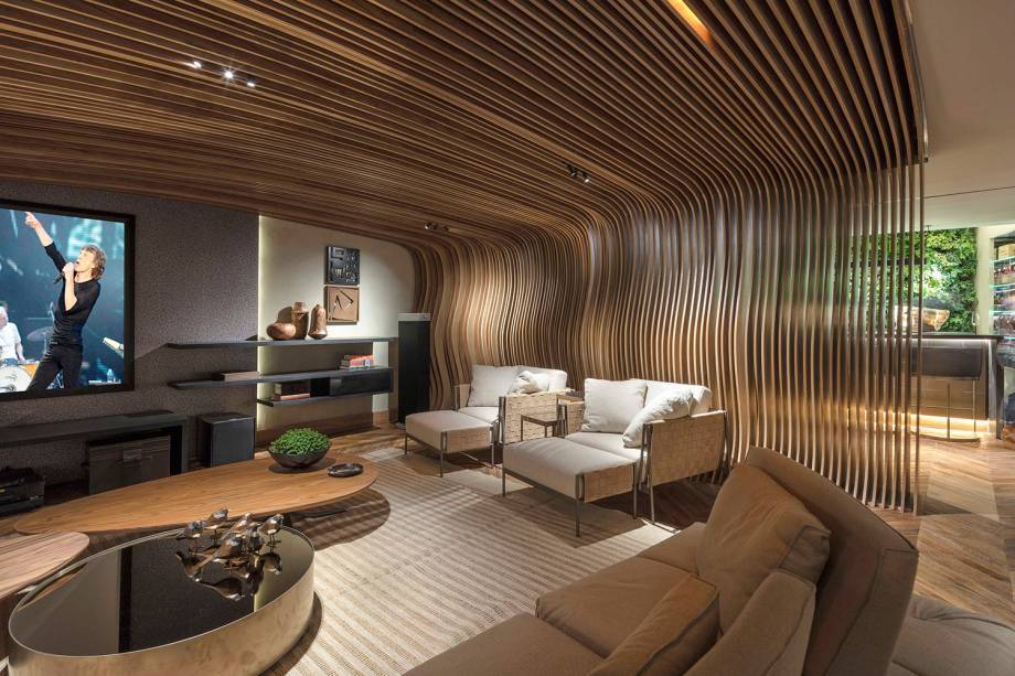 O ponto alto &eacute; a grande instala&ccedil;&atilde;o em madeira com desenho org&acirc;nico, que cobre o teto do home theater e desce na divis&oacute;ria vazada, que colabora para a qualidade ac&uacute;stica. No projeto de George Zardo e J&uacute;lia Zardo, o piso de madeira &eacute; uma composi&ccedil;&atilde;o de v&aacute;rias tonalidades e desenhos diagonais, em mais uma aposta no geometrismo.