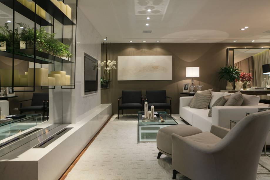 O painel da TV em m&aacute;rmore Ariston revela a nobreza intencional do projeto, assinado pela arquiteta Viviane Loyola, que tamb&eacute;m recebe uma marcenaria no tom Cafe Latte. As prateleiras suspensas em ferro e a mesa de centro em vidro trazem leveza.