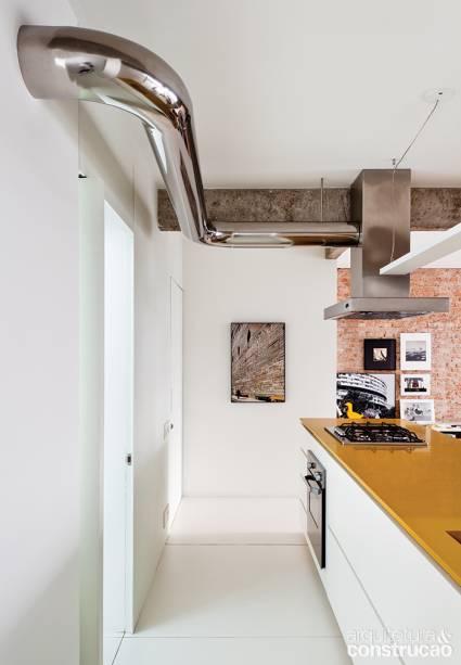 Projetada por Gabriel Kogan, esta cozinha imprime modernidade em cada detalhe. Na ambienta&ccedil;&atilde;o clean, as vigas de cimento queimado harmonizam junto ao grande fundo branco. O ar jovial ganha for&ccedil;a com o amarelo da bancada e tom metalizado da coifa