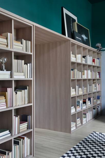 A <strong>Casa Berilo Leroy Merlin</strong>, assinada pelo Studio Ro+Ca, apresenta uma estante cujas cores contrastam com o verde esmeralda do ambiente. Assim como em todo o espaço, a estante também conta com linhas e formas bem definidas e abriga dezenas de livros.