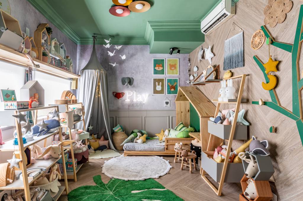 Espa&ccedil;o Conceito - Paula Carvalho. Pensado como um quarto para encantar crian&ccedil;as de todas as idades, este espa&ccedil;o funciona como uma loja e re&uacute;ne produtos de seis marcas de decora&ccedil;&atilde;o. Uma boiserie forra parte das paredes, o mesmo ocorre com um painel adesivo de estampa bot&acirc;nica. Dispostos por todo o ambiente, cestos e almofadas apresentam texturas aconchegantes e divertidas. Destaque para a cama casinha.