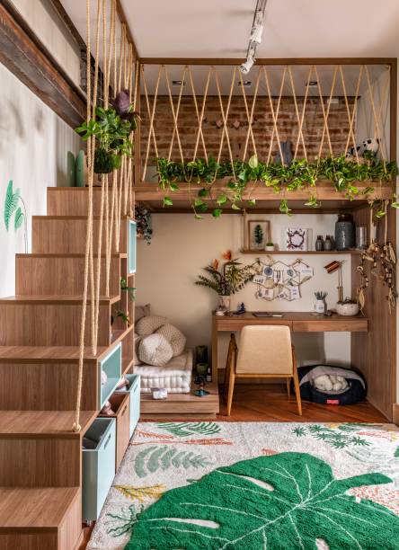 Home office - Studio Adoleta. Projetado em homenagem a mãe influencer Teca Toscano, este escritório aproveita cada cantinho dos 11 m² disponíveis. A marcenaria sob medida inclui um mezanino, um canto zen para meditação e uma bancada. Direcionado para os pequenos, há uma área para brincadeiras e leitura, reforçando o conceito multifuncional e prático do ambiente. Na parede, pintura artística da Manual Design.