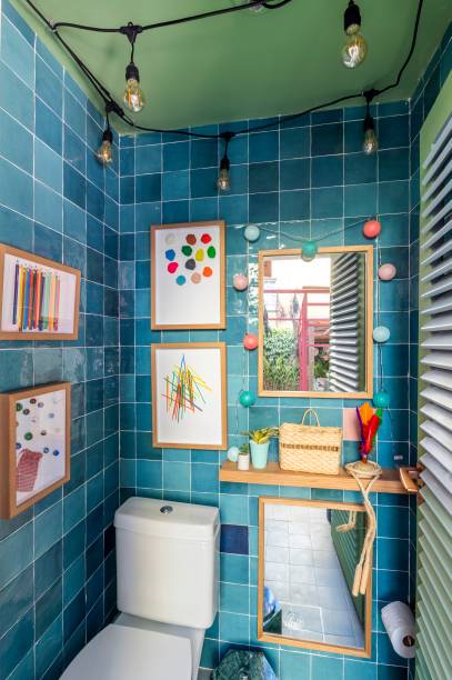 Lavabo Out - Isabela Fraia Arquitetura. As brincadeiras tradicionais ganham espaço neste projeto nada comum de banheiro. O espaço de 2m² celebra o universo lúdico e afetivo dos jogos da infância, como a peteca e a corda. A cerâmica azul reveste as paredes. No piso, uma amarelinha desenha o caminho até o lavado. Por conta do espaço reduzido, a bancada em granito foi deixada do lado de fora.