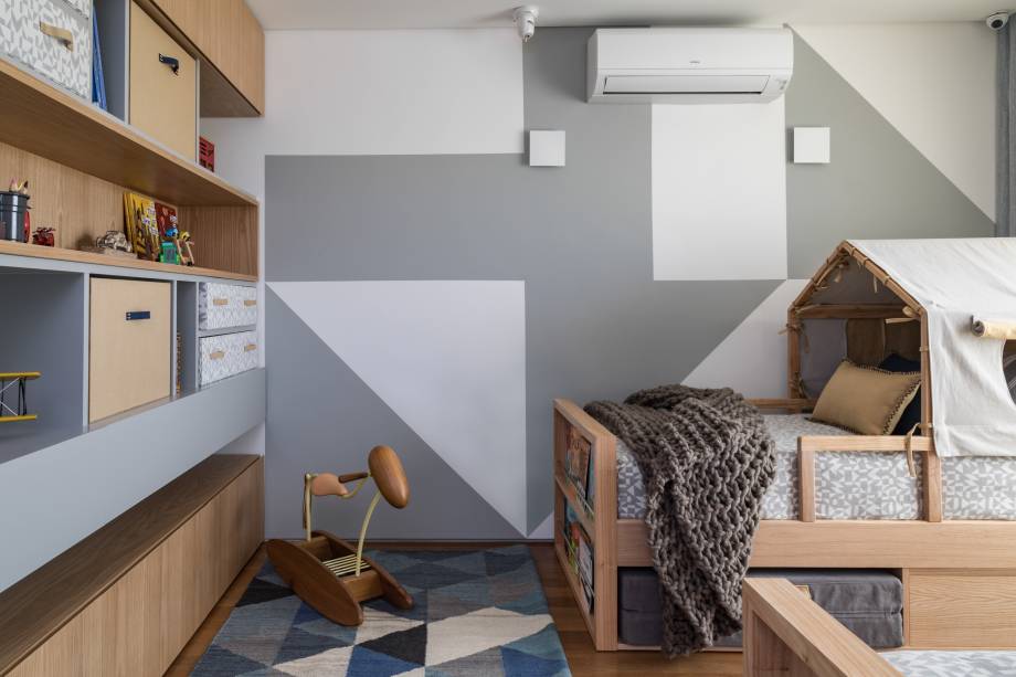 Um quarto lúdico, mas sem tema específico. Foi esse o pedido dos clientes desse projeto assinado pela Très Arquitetura. Com uma paleta de cores neutra em cinza e marinho, o destaque fica por conta da parede geométrica, que é propositalmente igual à estampa da colcha. O resultado é um quarto lúdico, aconchegante e que foge do comum.