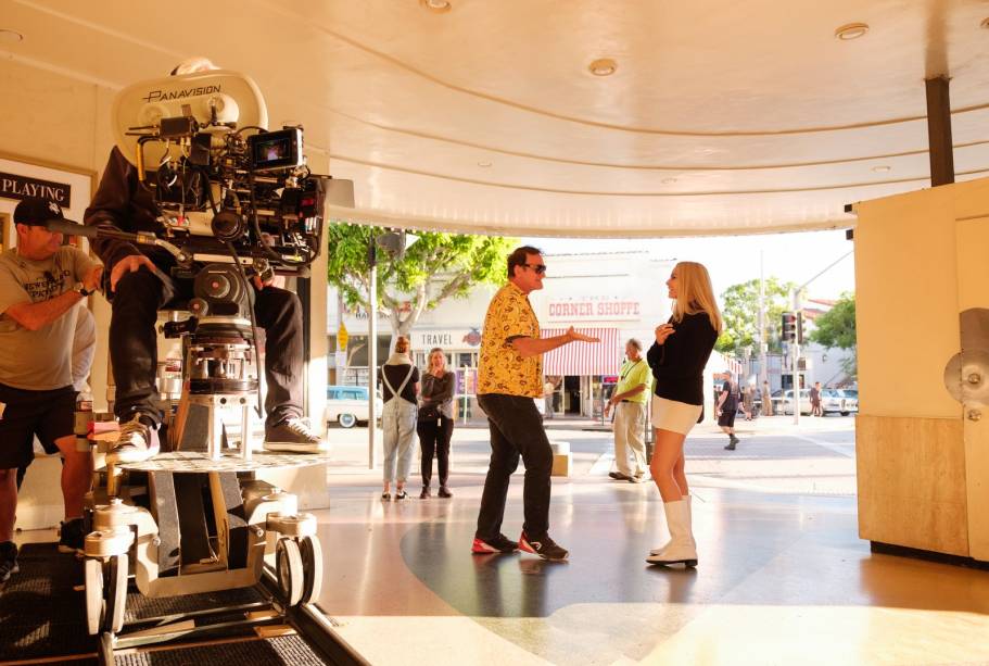 Era Uma Vez… em Hollywood – A Hollywood de 1969 formou o pano de fundo do escritor e diretor Quentin Tarantino. Era Uma Vez ... em Hollywood retrata a vida de um astro de cinema frustrado que interpreta cowboys, Rick Dalton (Leo DiCaprio), seu companheiro e dublê (Brad Pitt) e sua vizinha Sharon Tate (Margot Robbie). O filme é uma viagem de máquina do tempo de Tarantino aos lugares que ele lembrava de sua infância em Los Angeles, dos icônicos Cinerama Dome e Musso & Frank's no Hollywood Boulevard aos estúdios ocidentais do estúdio e o cenário do show de variedades dos anos 60, Hullabaloo. A estilista Barbara Ling (que também cresceu em Los Angeles) recebeu as dicas do diretor e eles compartilharam um sentimento de nostalgia e cultura pop. “É a carta de amor de Quentin para a cidade em que ele cresceu”, ela diz, “sendo uma enciclopédia absoluta de filmes, Quentin exibiu filmes como The Wrecking Crew, Valley of the Dolls e Bob & Carol & Ted & Alice em seu move theater uma vez uma semana para nós. "Trabalhando com a decoradora de cenários Nancy Haigh, eles criaram cerca de 150 cenários, incluindo as casas da Playboy Mansion, Tate e Dalton em Hollywood Hills, no meio do século, bem como a casa da família Manson no agora extinto Spahn Movie Ranch. Tarantino até forneceu recordações de sua vasta coleção para a casa de fazenda de Dalton. "Quentin tem essa coleção de pôsteres de filmes muito rara e magnífica que usamos para a decoração", observa Ling. "Ele tinha peças muito específicas e fez suas próprias decorações pessoais, como a xícara Hopalong Cassidy". Na foto, Quentin Tarantino dirige Margot Robbie (que interpreta Sharon Tate) durante uma filmagem no local.