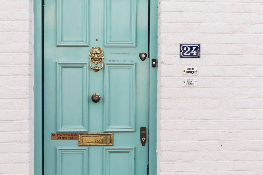 como-calcular-a-numerologia-da-casa Fachada de uma casa com porta verde-água, parede de tijolinhos brancos e número 24
