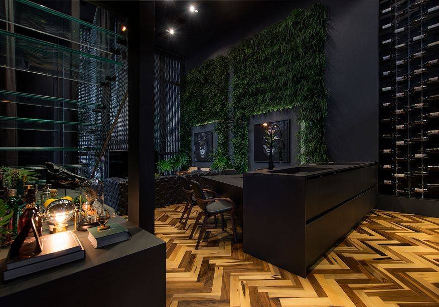 CASACOR Santa Catarina Itapema. Loft do Arquiteto - Athos Peruzzolo. O piso em madeira e o jardim vertical criam um ref&uacute;gio e quebram a sobriedade do ambiente de 100 m&sup2;. A cor preta &eacute; protagonista, ressaltando a volumetria e o design do mobili&aacute;rio fixo e da estrutura do espa&ccedil;o. V&aacute;rios elementos exploram a verticalidade, como a escada com degraus em vidro e, do lado oposto, a parede transformada em adega.