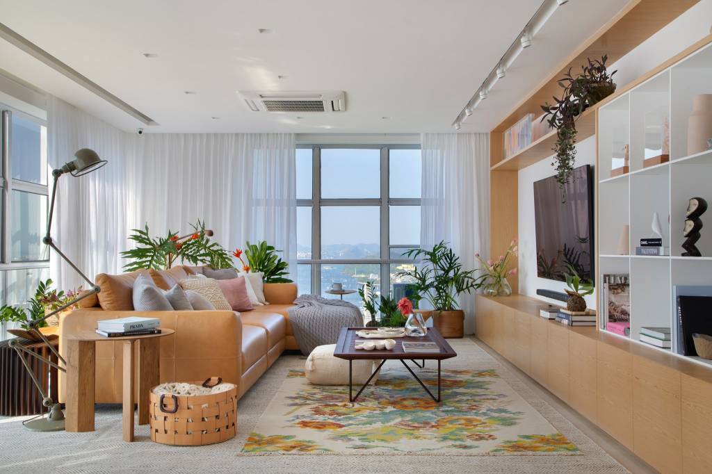 apartamento-marina-romeiro-rio-vista-mca-estudio-01 Estar com vista para o mar. Tapete florido. Estante em madeira com nichos brancos. Sofá de couro amarelado