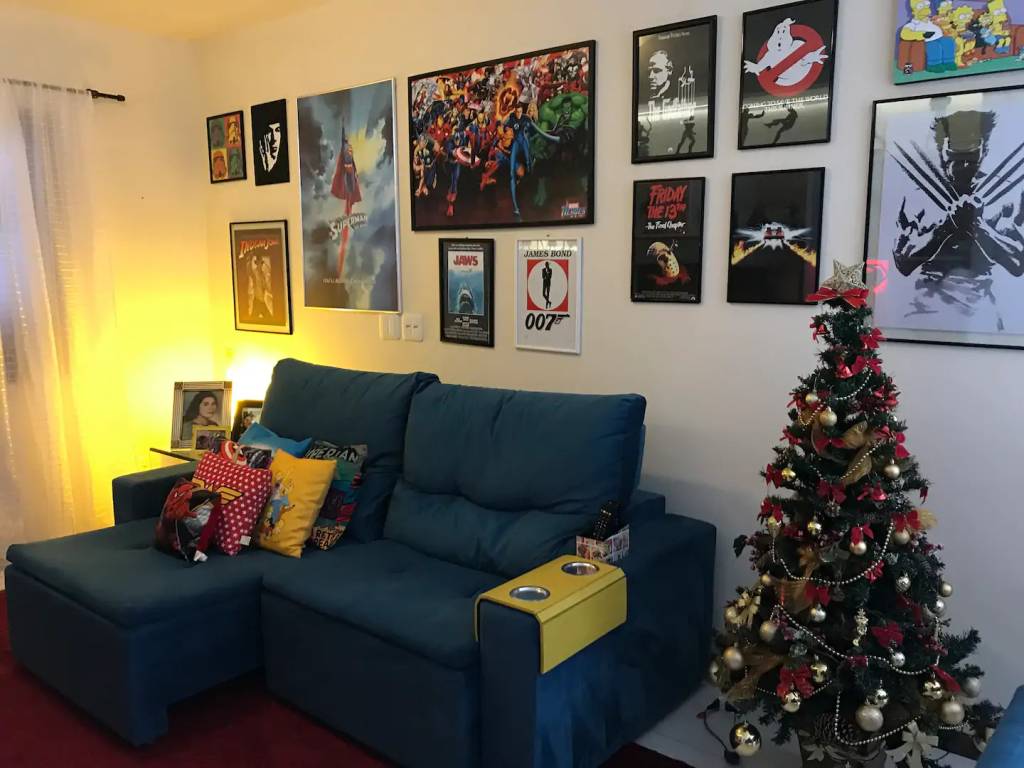 casas-tematicas-do-airbnb-no-brasil-hobbits-herois-e-amantes-de-vinho-casa.com-6-super-herois Sala com sofá azul com parede decorada com quadros temáticos de super heróis em tamanho diferentes