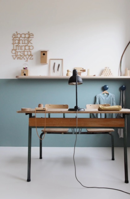 Home office com parede meia colorida em azul. Quadros na prateleira de madeira que marca a divisão entre a parte azul e a parte branca da parede. Mesa em madeira.