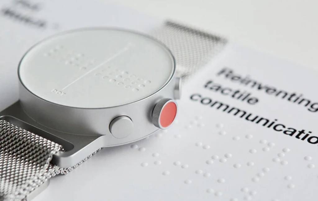 Detalhe do mostrador do Dot watch. Com manual em braille na mesa