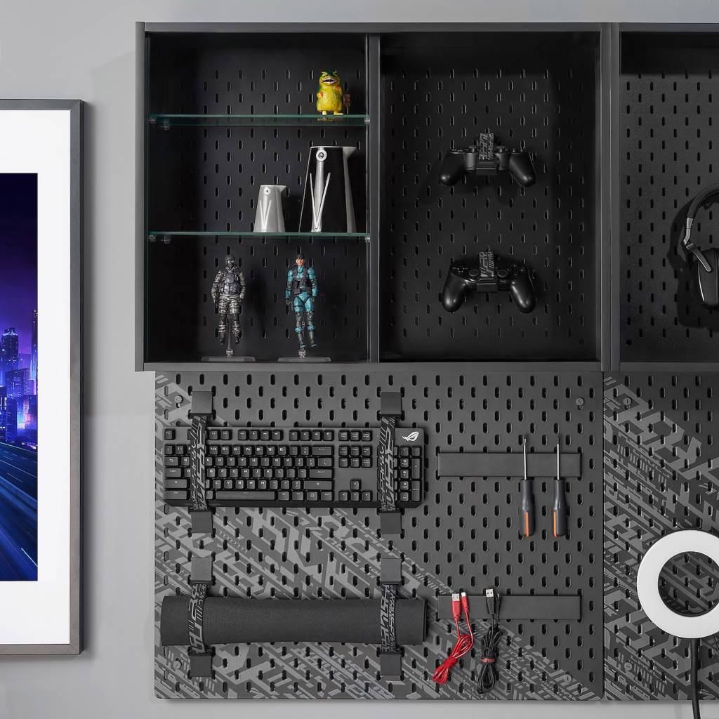 ikea-lanca-colecao-de-moveis-para-e-sports-casa.com-5 Um mural preto com teclado, mousepad e ferramentas presos a ele com fita. Acima, nichos estão decorados com figuras de ação e controle de video game