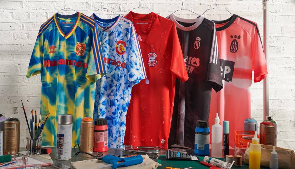 pharrell-williams-lanca-linha-de-produtos-de-skincare-pela-humanrace-casa.com-7-camisas-adidas Cinco camisas de times de futebol europeus, coloridas e penduradas em uma arara.