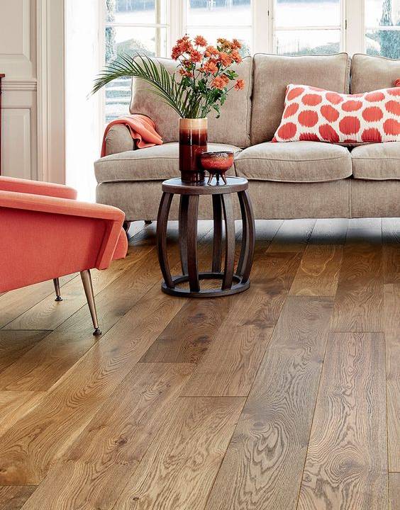 Sala de estar com sofá, decoração com detalhes em laranja e piso laminado.