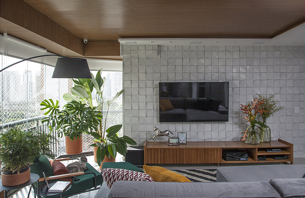 Sala de TV com revestimento cinza 3d. Luminária de chão sobre poltrona verde. Plantas no canto do cômodo