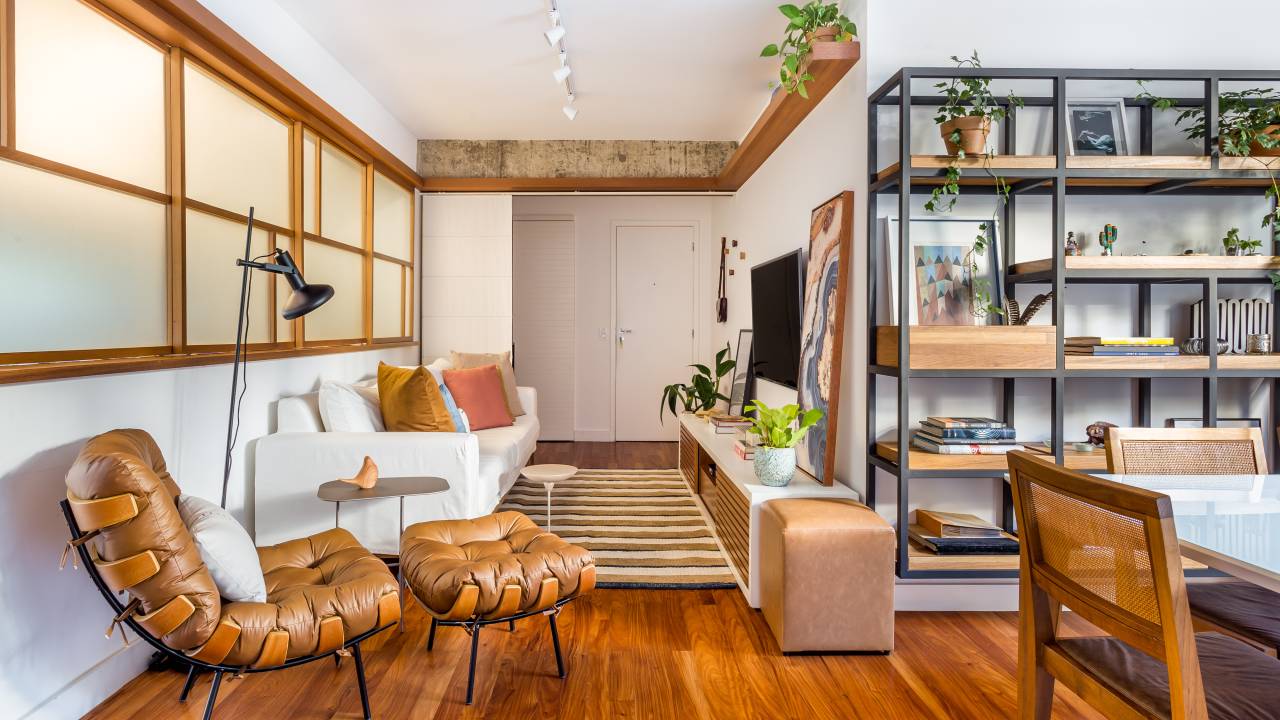 Sala de estar com piso de madeira e décor neutro, estante no estilo industrial, sofá branco e poltrona marrom