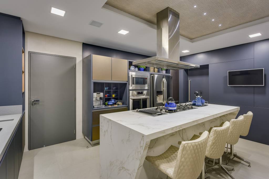5-dicas-para-a-cozinha-perfeita-casa.com-1 2017©Nenad-AlessandraGandolfi-2101-2-EditarAlta Cozinha com armários azul escuro pastel, e eletrodomésticos em inox. No centro, uma ilha com cooktop em pedra branca, com cadeiras na mesma cor