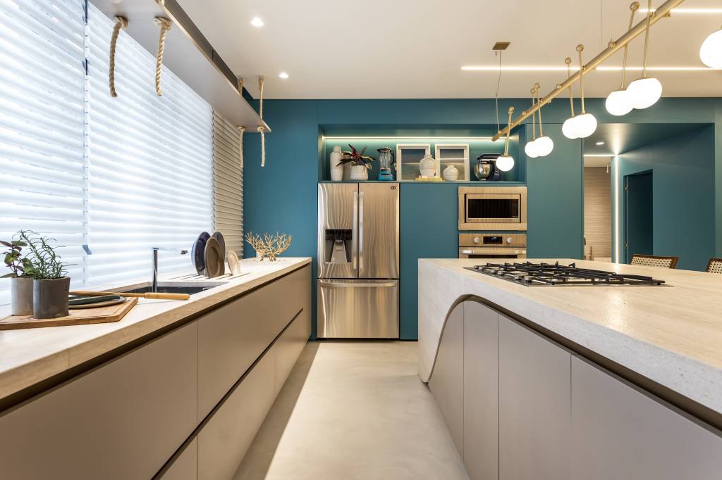 Cozinha com armários azuis, eletros em inox e bancada com armários cinzas embaixo, com cooktop