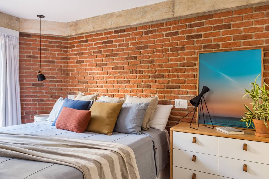 7-apartamento-terreo-de-163-m-2-ganha-estilo-industrial-e-toques-praianos Quarto de casal com parede revestida por tijolinhos e escrivaninha branca com madeira