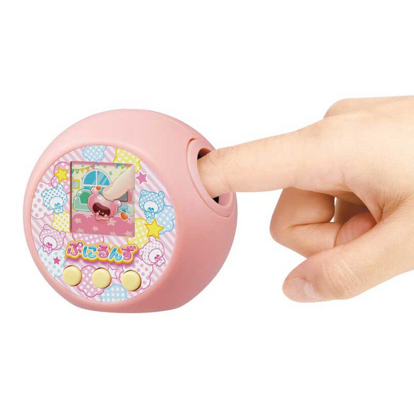 agora-voce-consegue-fazer-carinho-no-seu-tamagochi-casa.com-designboom-takara-tomy-3 O brinquedo na cor rosa, aparece com um dedo ilustrando o diferencial do produto