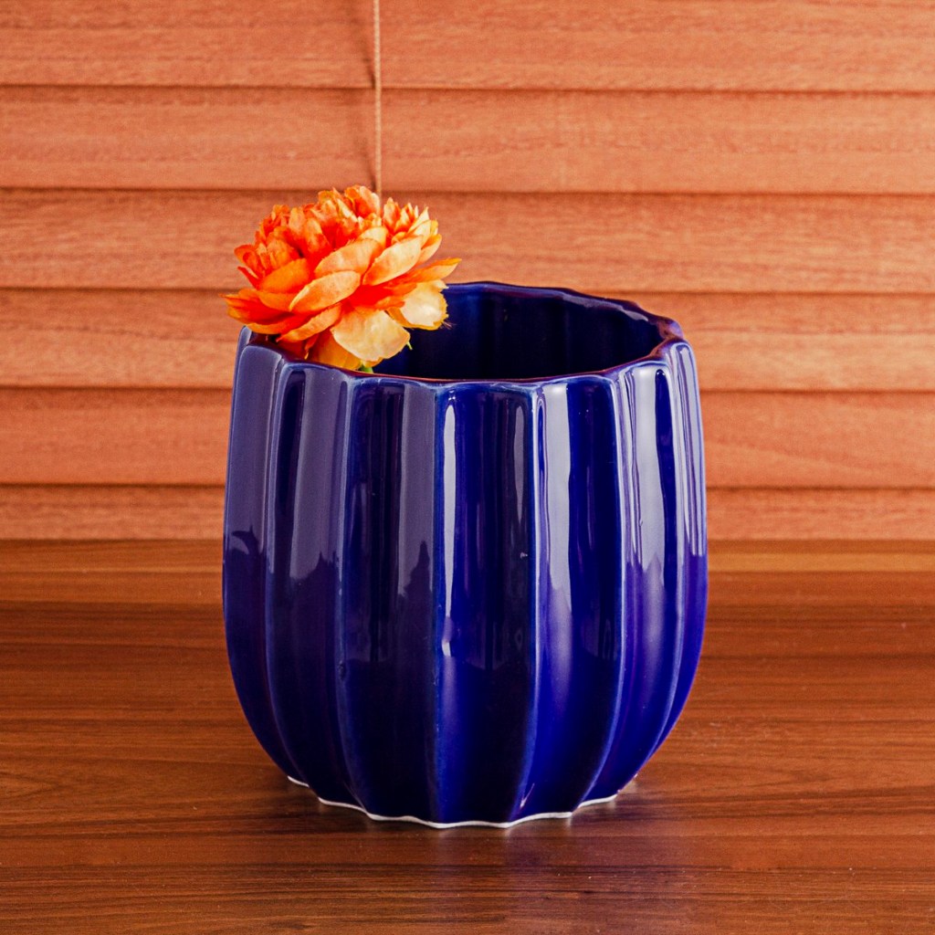 Vaso de cerâmica azul, com flor laranja sobre bancada de madeira
