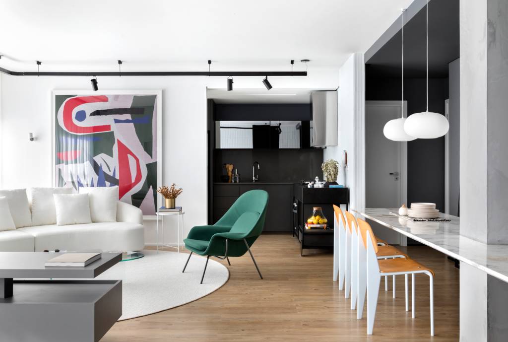 estudio-de-73-m²-com-planta-integrada-e-design-moderno-casa.com-archdaily-studio-gabirel-bordin-fabio-junior-severo-2 Sala de estar com piso de madeira,com tapete redondo branco no centro,sob sofá da mesma cor. Ao lado, uma poltrona verde, com uma mesa de janta branca, com detalhes em madeira. no teto, trilho de holofotes e na parede, uma obra de arte abstrata